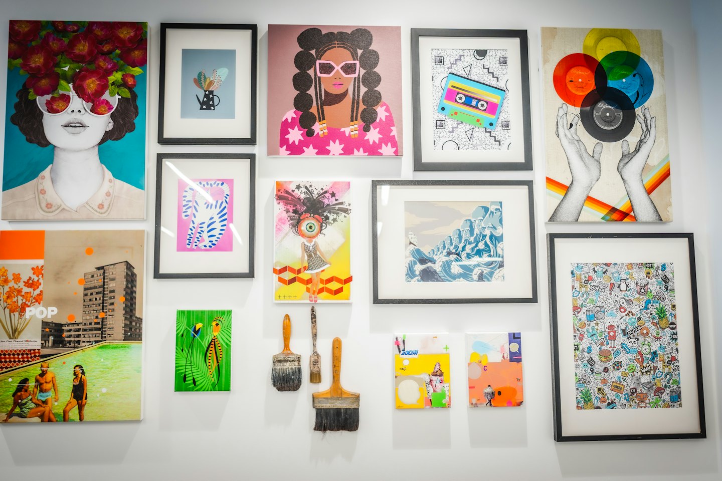Bunte Sammlung zeitgenössischer Kunstwerke und Pinsel an einer Galerie-Wand.